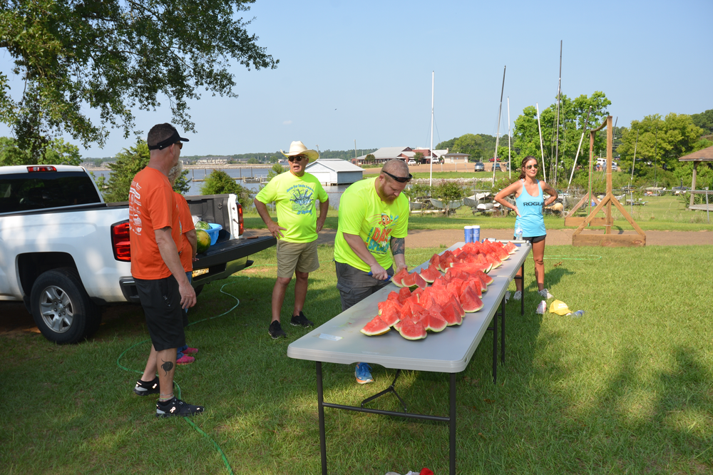 A group of people are standing around a table filled with watermelon slices.
