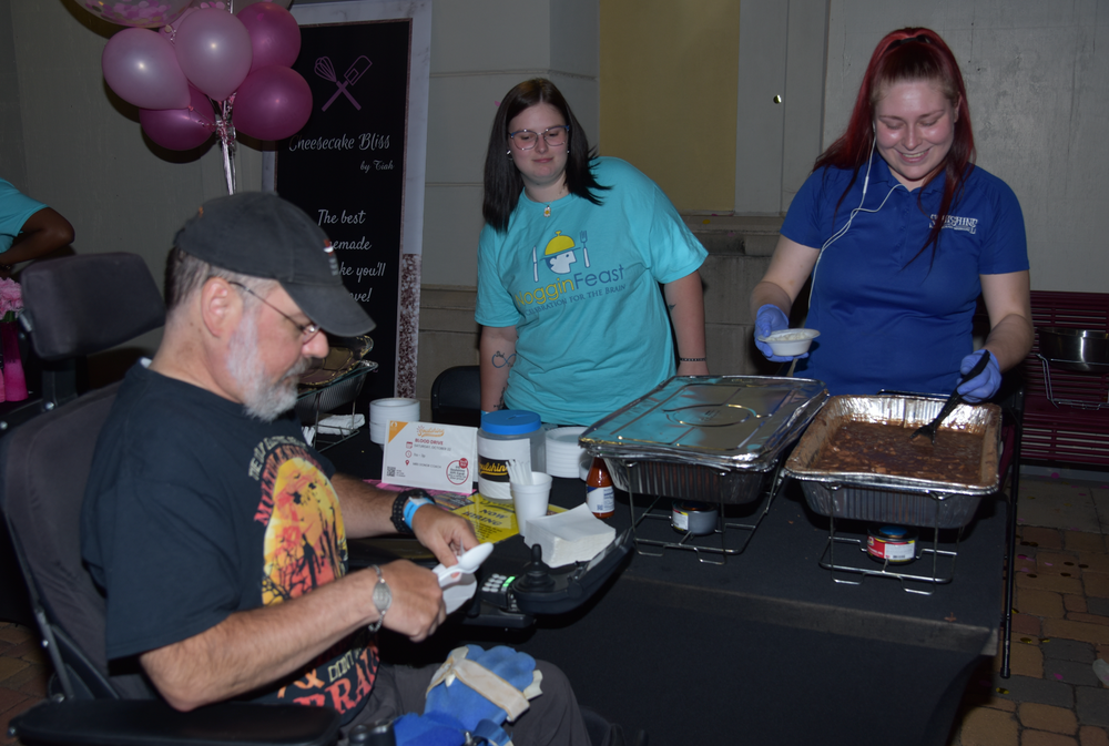 A man in a wheelchair is sitting at a table with two women serving food.