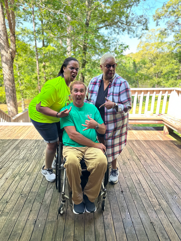 A man in a wheelchair is standing next to two women on a deck.
