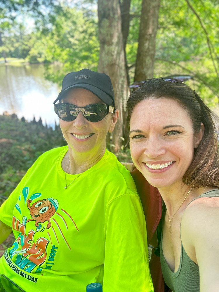 Two women are posing for a picture while sitting next to each other in front of a lake.