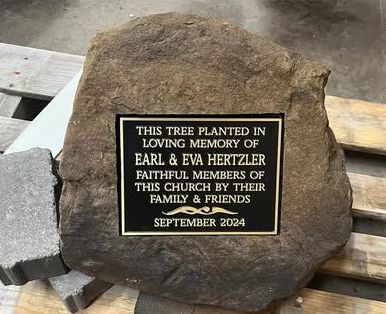 A stone with a plaque on it that says `` this tree planted in loving memory of earl & eva hertzler ''