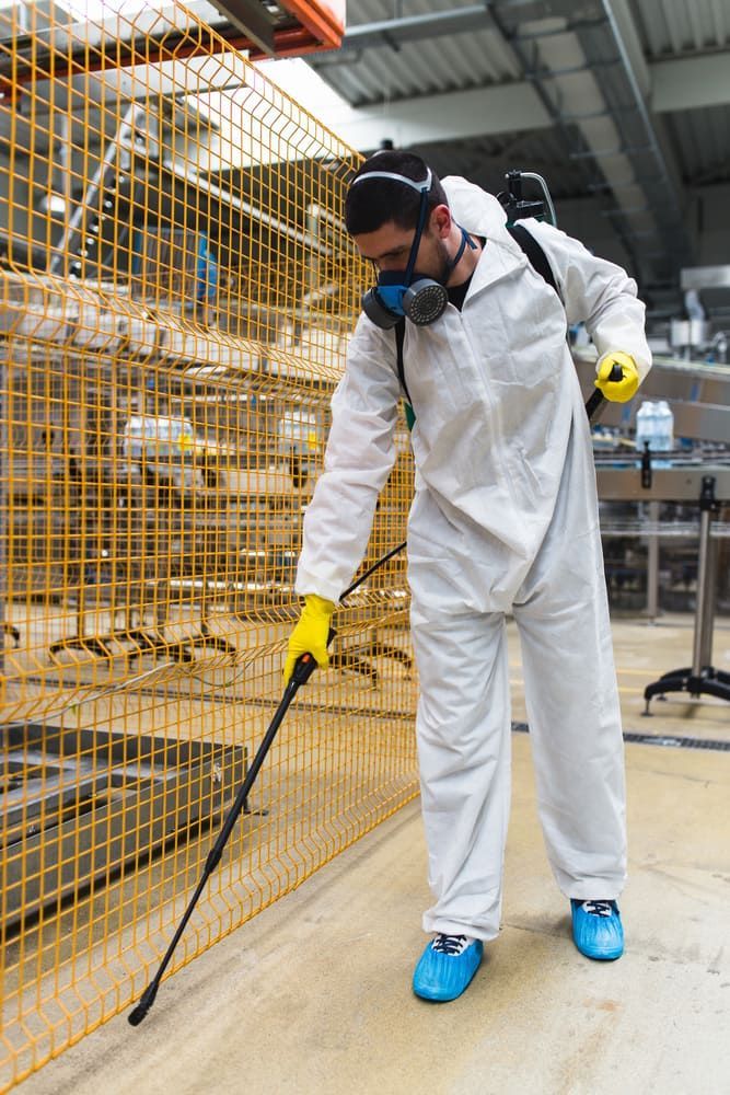 A Man In A Protective Suit Is Spraying A Warehouse With A Sprayer — Maximum Pest Management In Mareeba, QLD