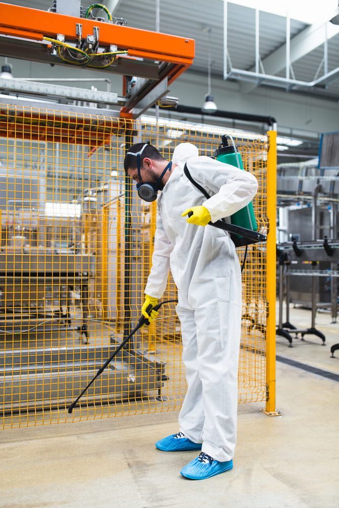 A Man In A Protective Suit Is Spraying A Machine In A Factory — Maximum Pest Management In Mareeba, QLD