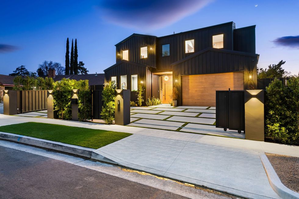 Modern two-story house with lit entryway, landscaped yard, and a paved driveway at dusk