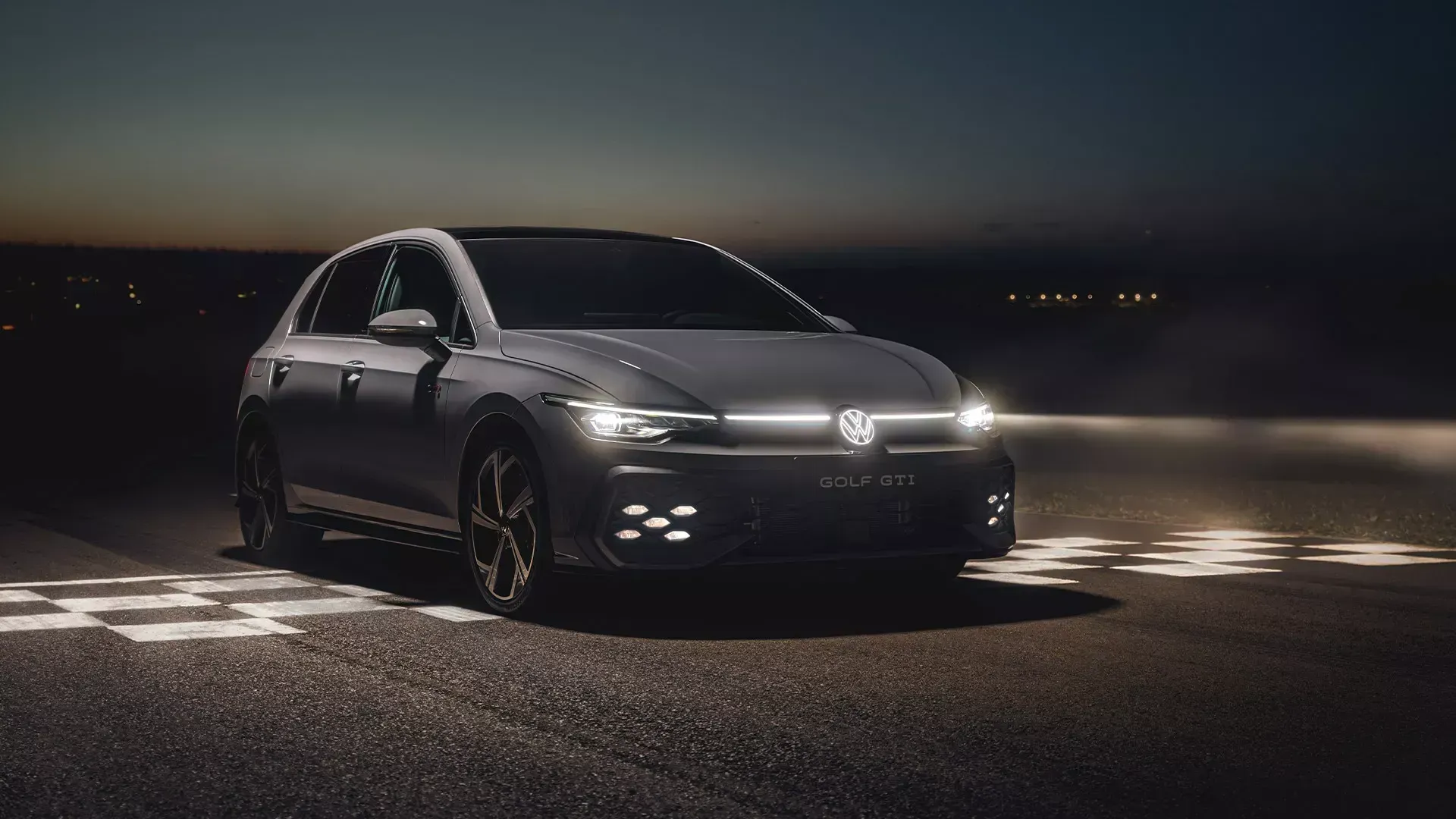 Sedan preto com faróis acesos, dirigindo em uma estrada mal iluminada à noite.