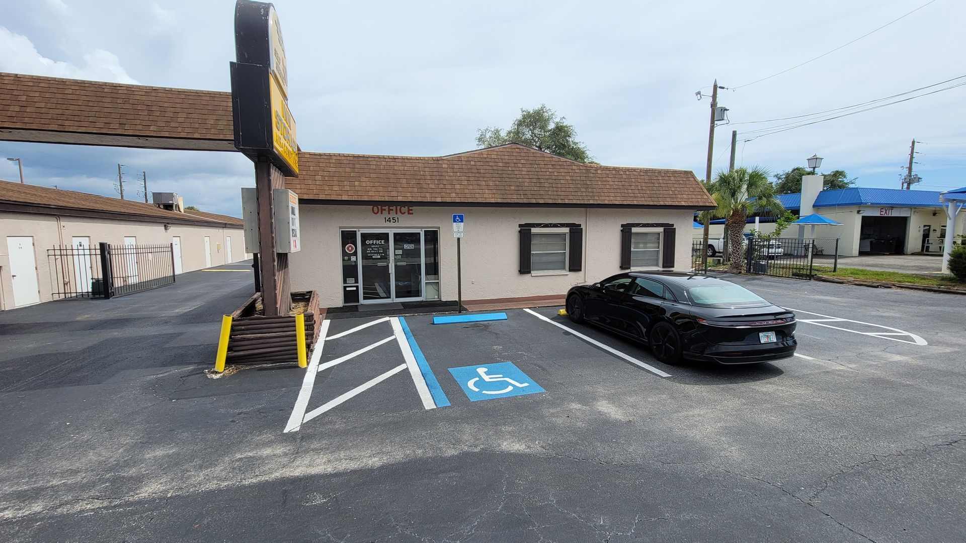 Small parking lot with accessible spaces beside a low building and a black car.