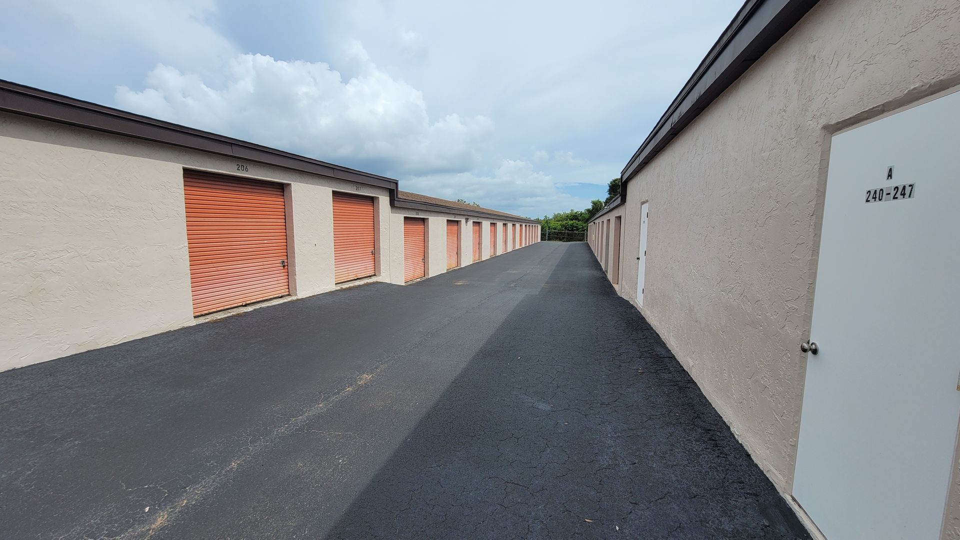 Narrow alley between storage garages with orange doors and a white side door under cloudy sky