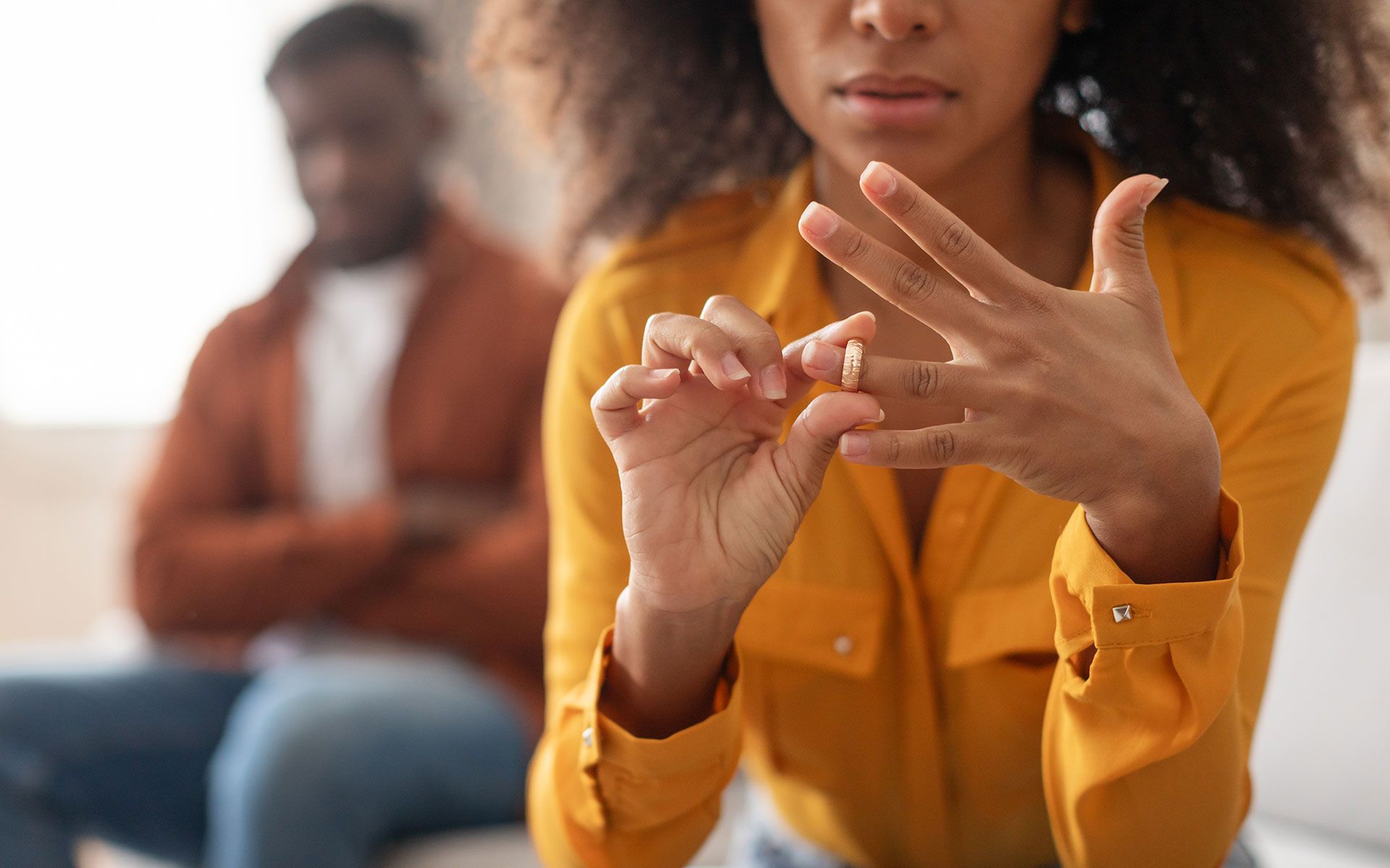 Woman removing wedding ring, man in background, suggesting divorce.