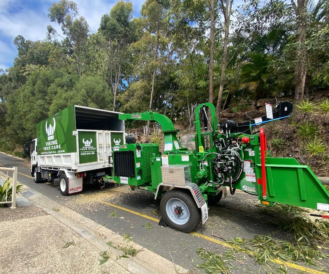 Green wood chipper and dump truck parked roadside in a wooded area