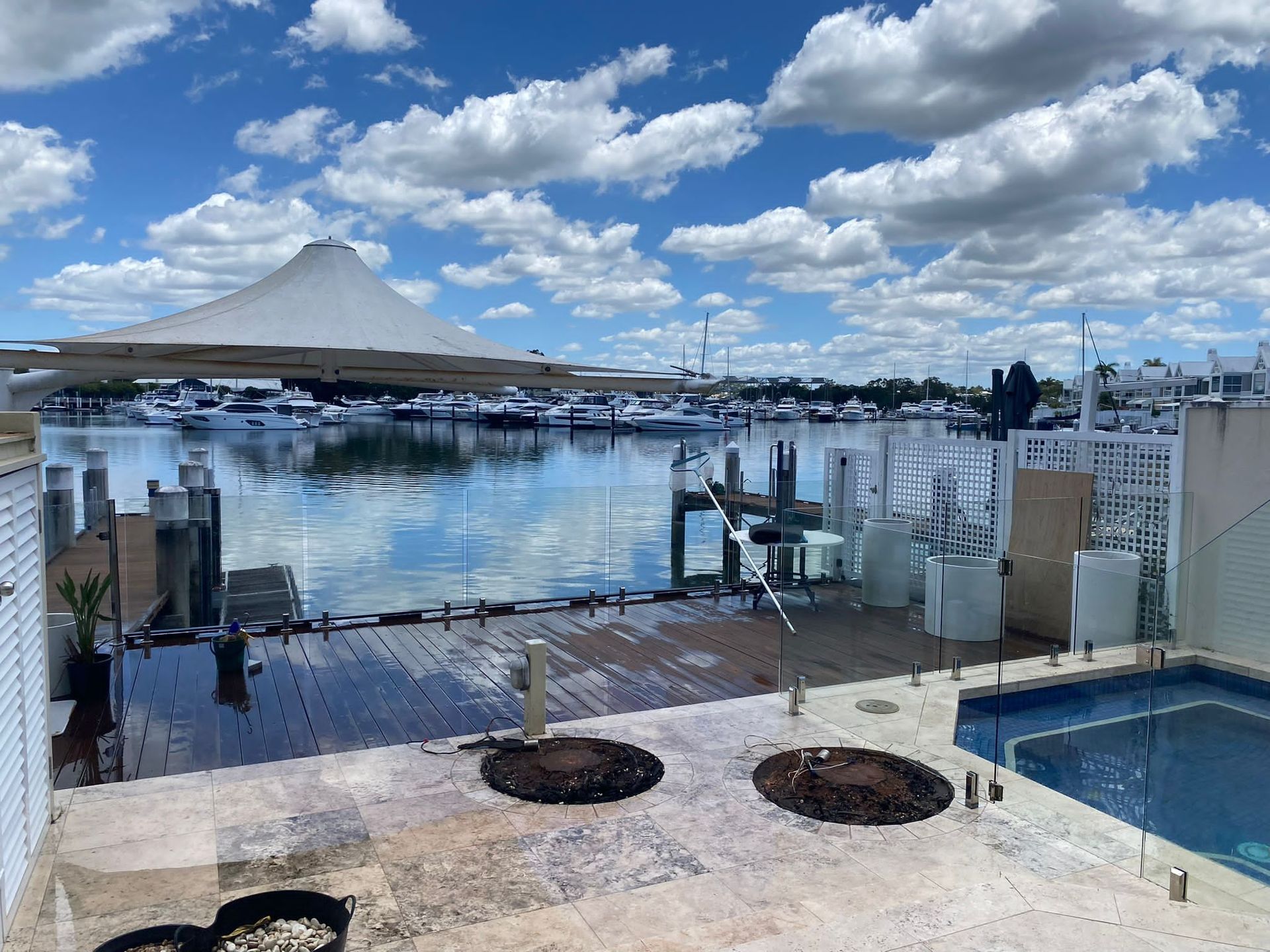 Marina waterfront with boats, calm water, a pool, and cloudy blue sky.