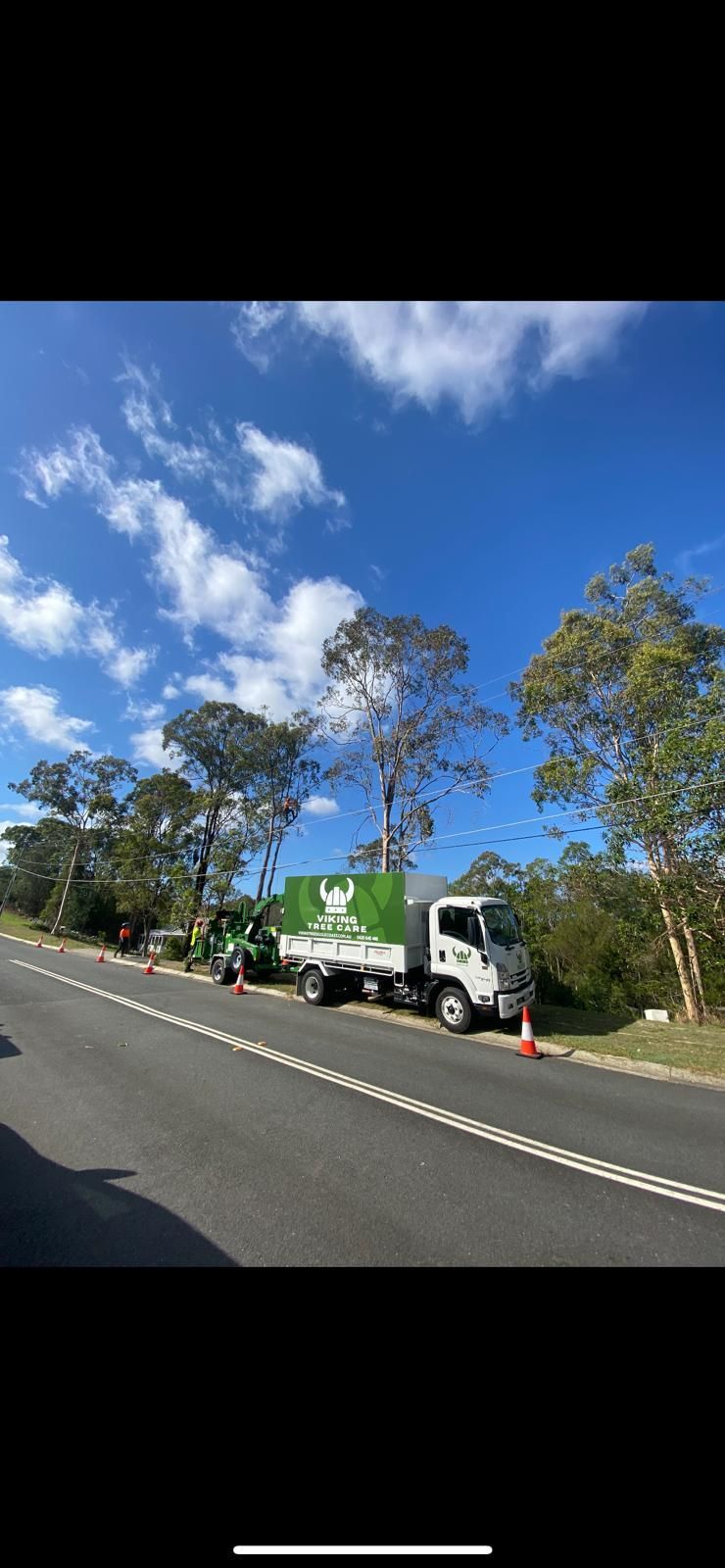 White truck parked on roadside with orange cones, beside a green building under a bright blue sky