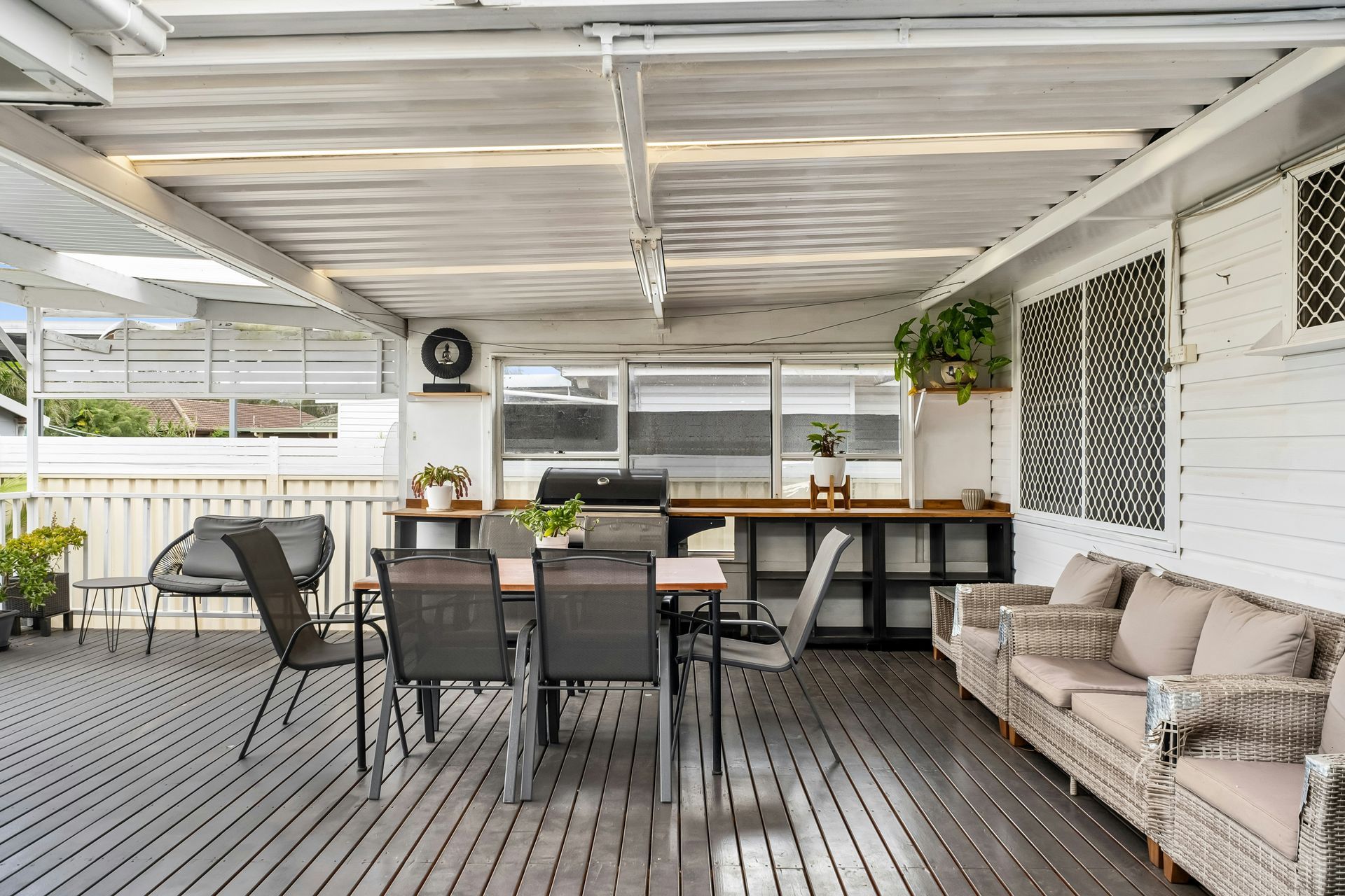 Covered patio with outdoor dining table, wicker chairs, and a beige sofa on a gray deck.