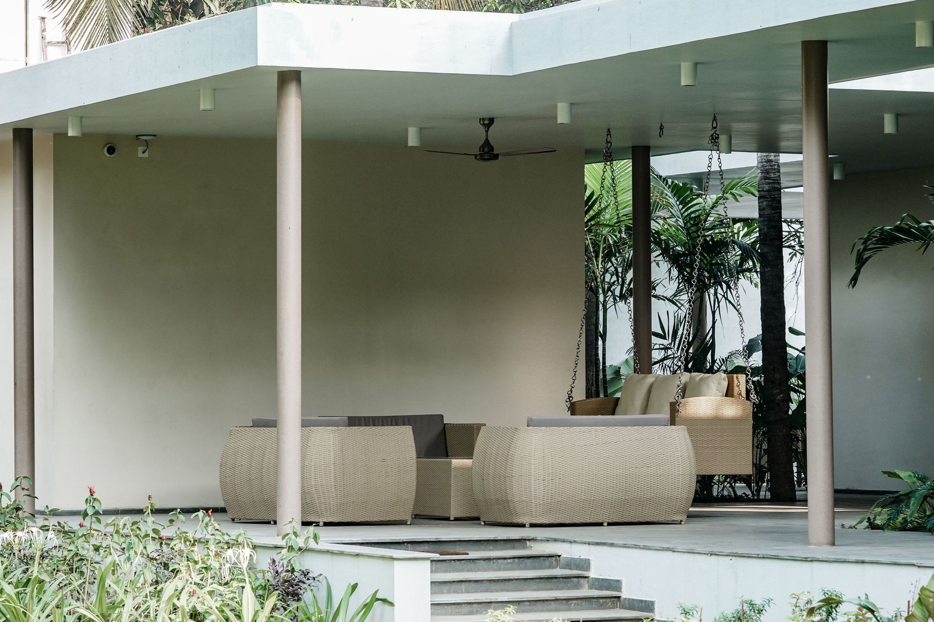 Covered outdoor patio with wicker seating and potted plants in a modern building