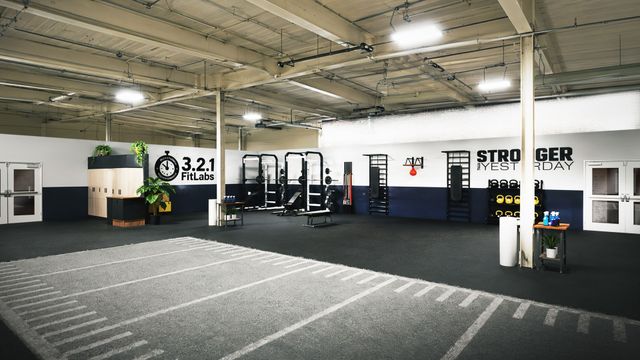 Empty gym with black flooring, squat racks, and STRONGER branding on the walls