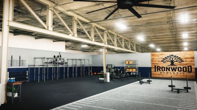 Empty industrial gym with black flooring, weight equipment, and a large “Ironwood” banner on the wall