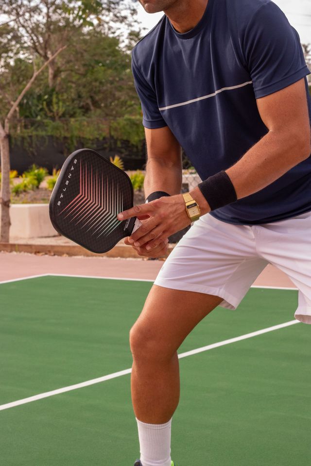 Person holding a pickleball paddle on an outdoor court, wearing navy shirt and white shorts.