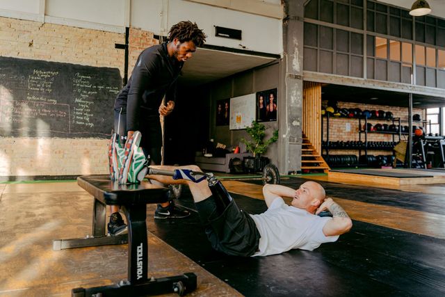 Person doing a floor exercise while a trainer stands nearby in a gym