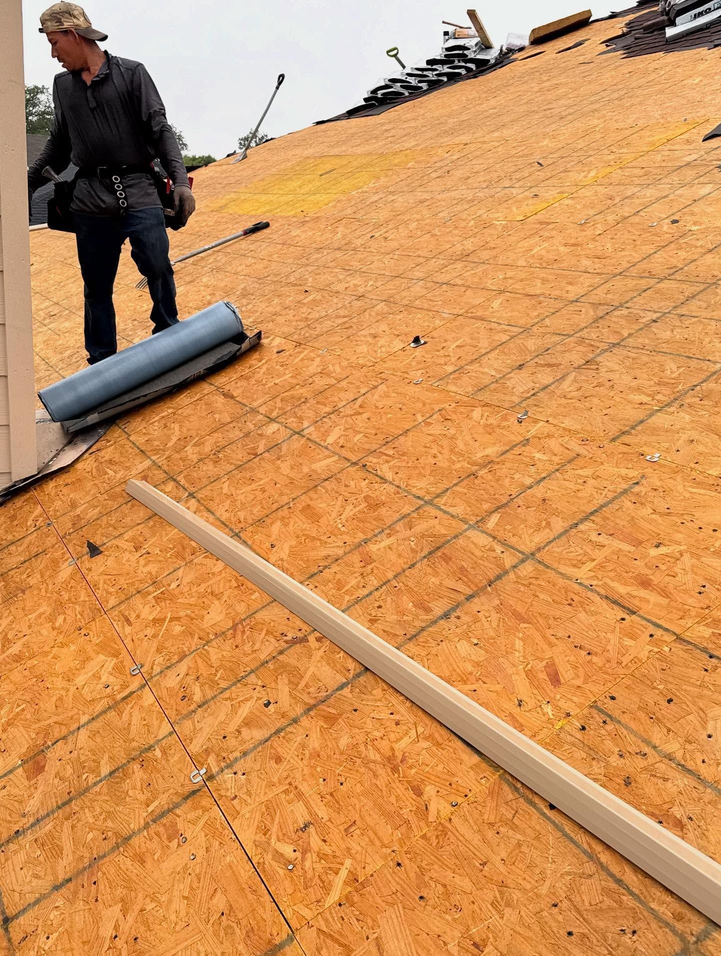 A man is standing on a roof holding a roll of plywood.