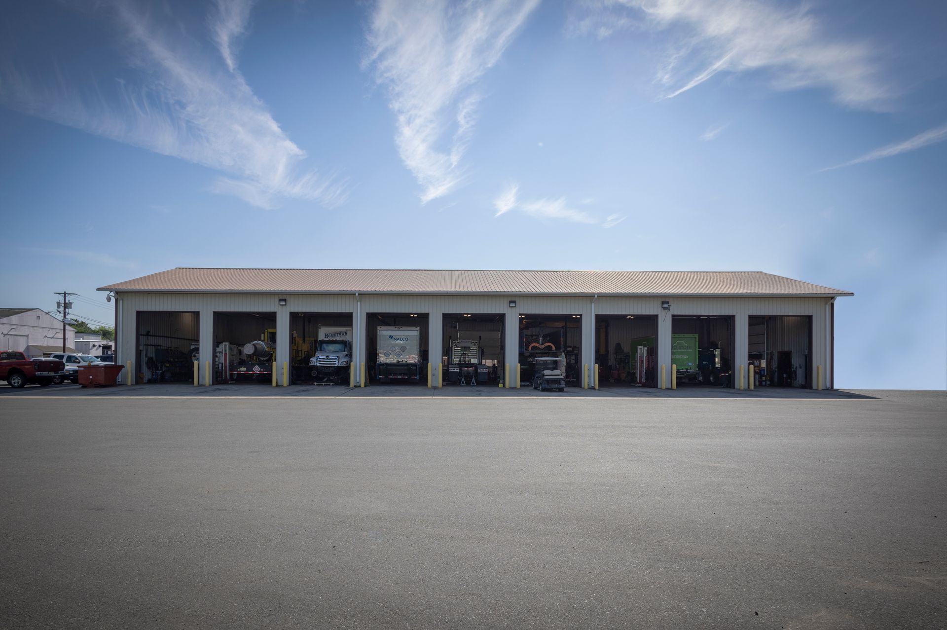 Exterior view of a repair shop with multiple garage bays, set against a blue sky with streaky clouds.