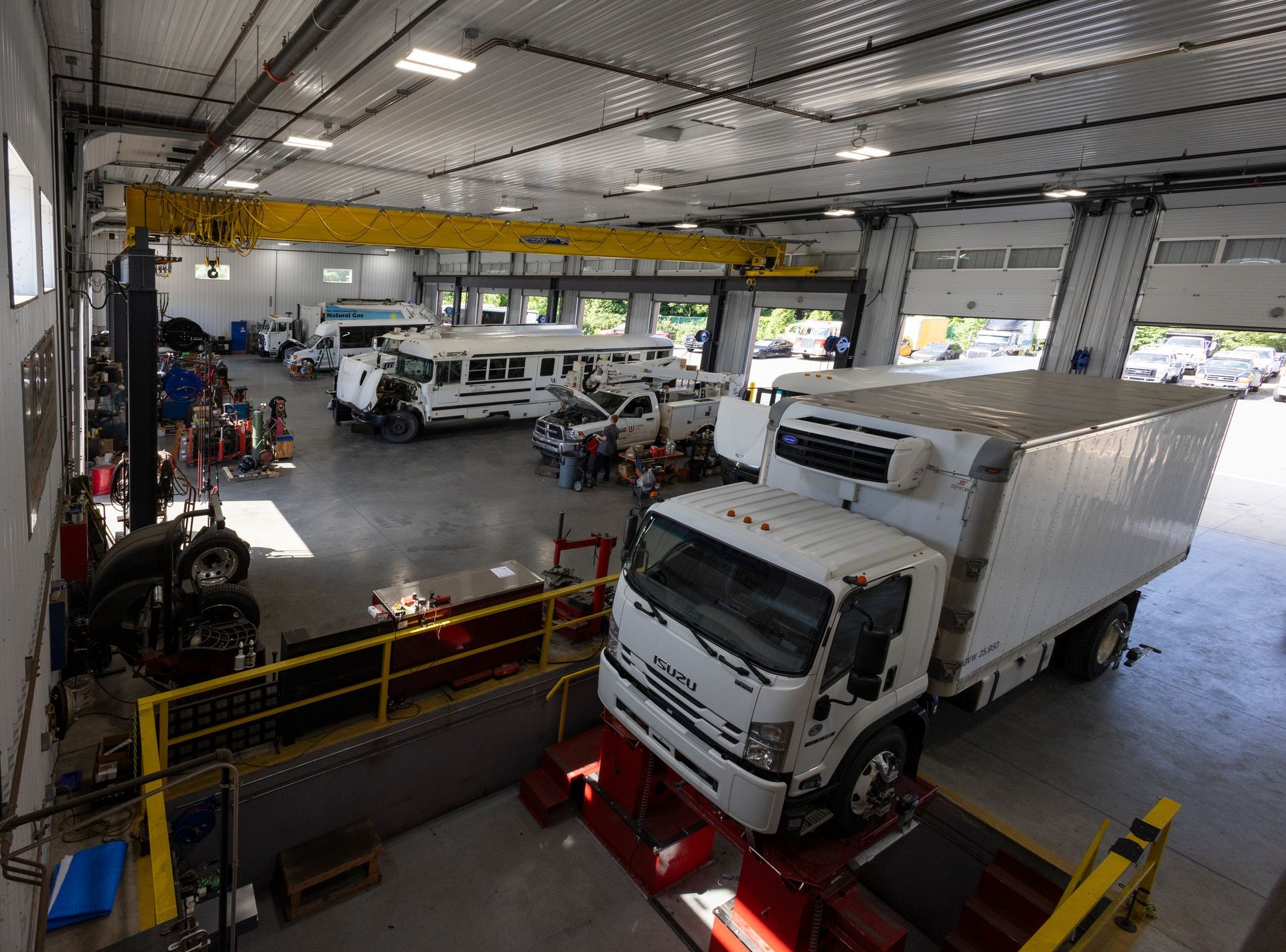 Truck repair shop, a large white truck is on a lift, other vehicles and people in the background.