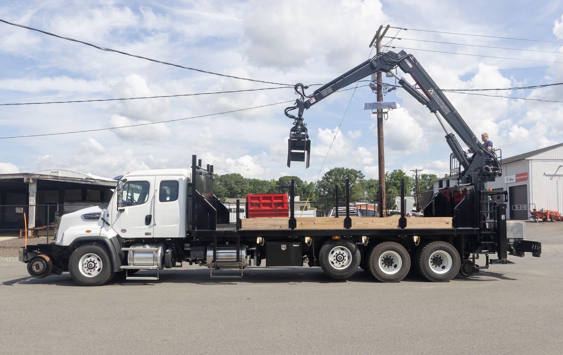 White flatbed truck with crane arm lifting a grapple.