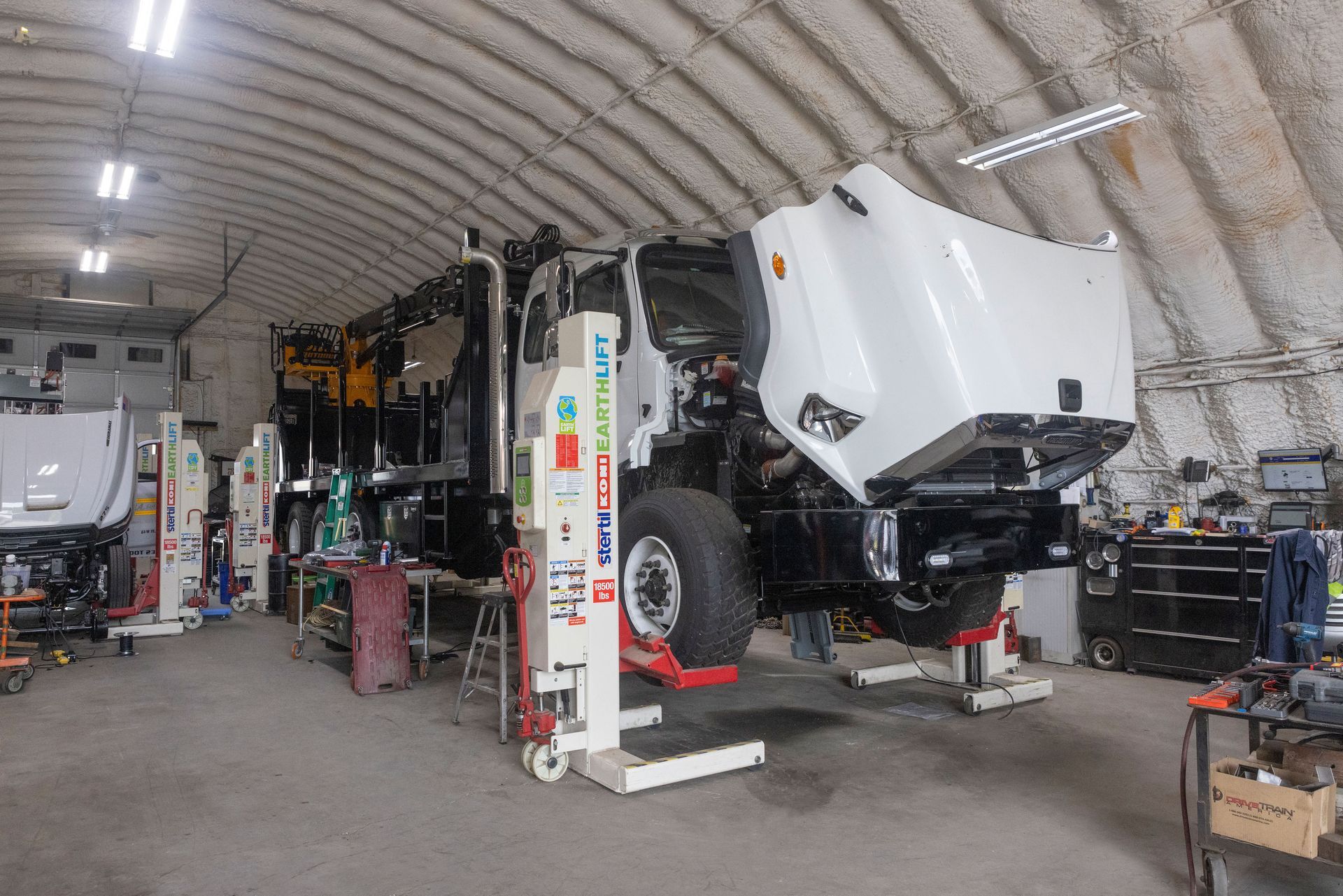 Truck cab in a repair shop with the hood open, raised on jacks.