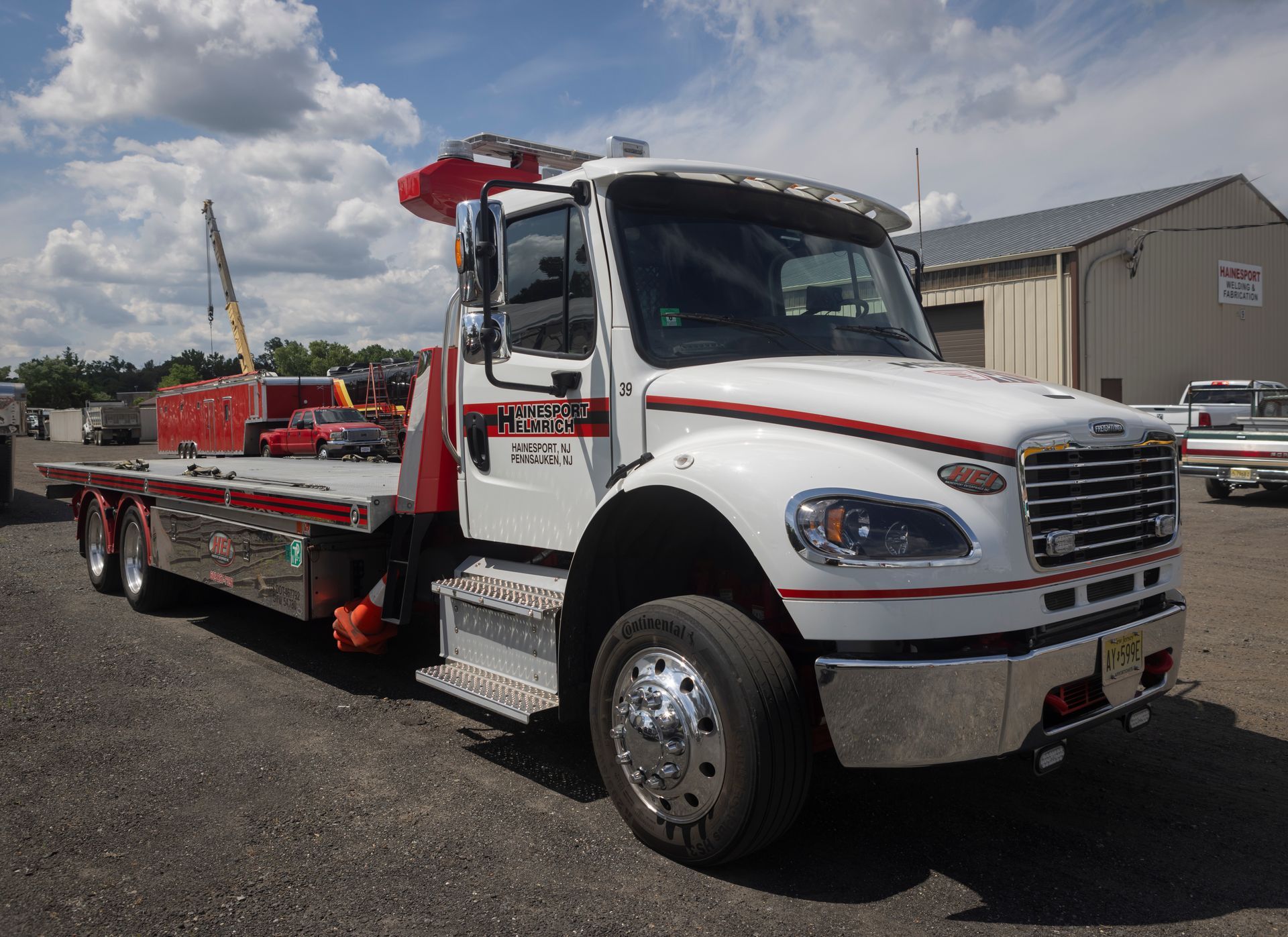White tow truck with a flatbed, parked outdoors under a bright sky.