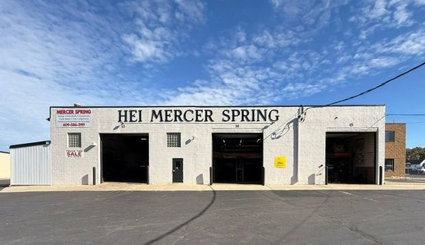 White building with large garage doors, HEI MERCER SPRING sign, blue sky.