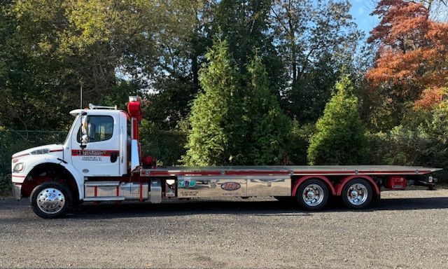 White and red tow truck with a flatbed in front of trees.