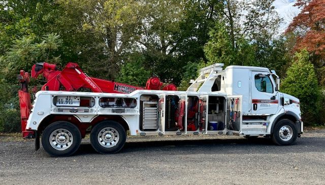 White and red tow truck parked on asphalt; trees in background.