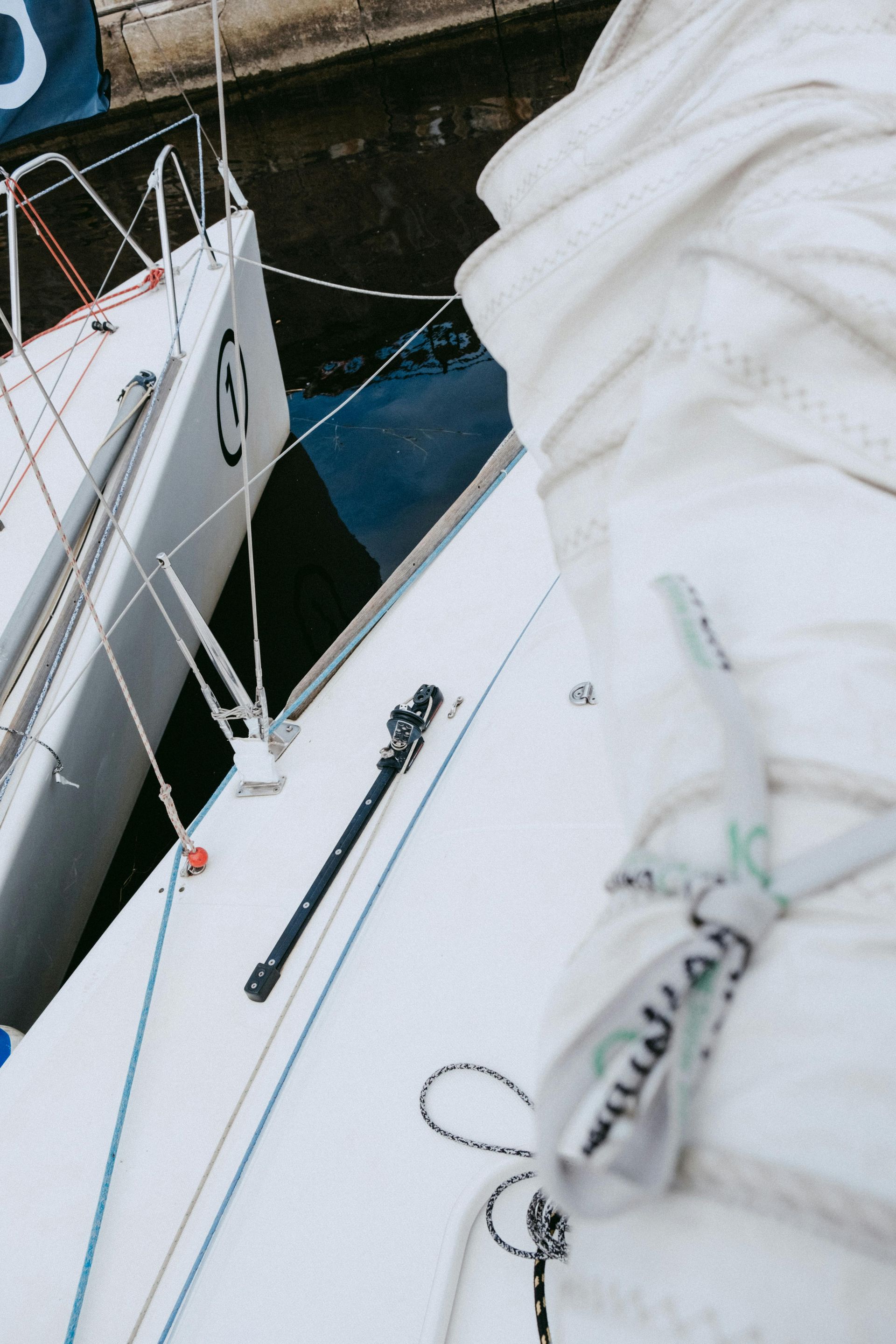Two white sailboats docked next to each other, one with sails furled, close-up of deck.