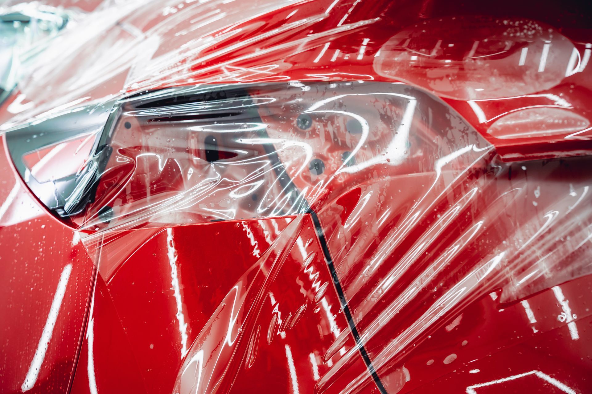 Red car's surface covered in clear protective film during installation process.