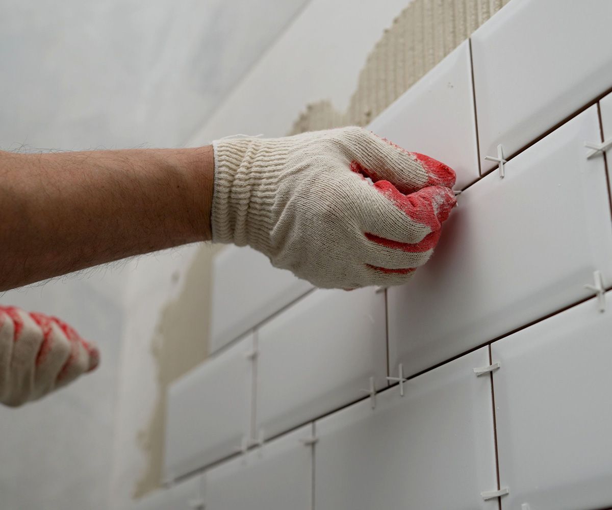 Worker Lay Ceramic Tiles on the Kitchen Wall — Omaha, NE — Lewis Tile Installations Worker Lay Ceramic Tiles on the Kitchen Wall — Omaha, NE — Lewis Tile Installations