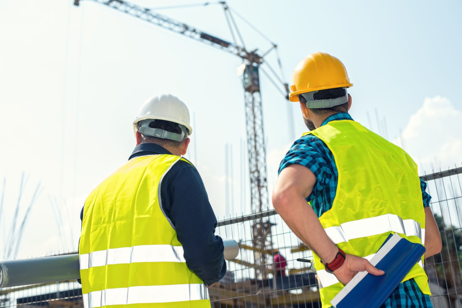 Due operai edili con giubbotti di sicurezza e caschi protettivi osservano un cantiere con una gru.