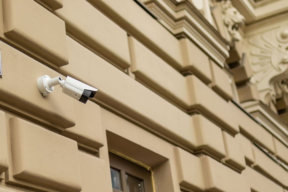 Telecamera di sicurezza montata sull'esterno di un edificio beige con dettagli architettonici.