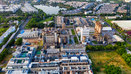 Aerial view of a large industrial plant with smokestacks beside a lake and surrounding greenery