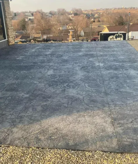 Flat rooftop covered with dark roofing material, overlooking a distant neighborhood