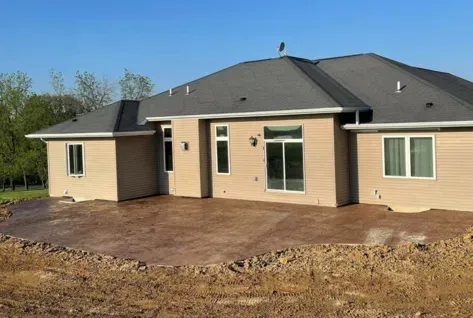 New beige house with dark roof and a large concrete patio in a dirt yard