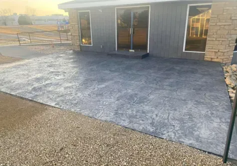 Concrete patio beside a dark house with sliding glass doors and stone siding at sunrise