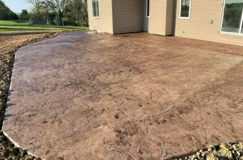 Stamped concrete patio beside a beige house, with a curved edge and surrounding lawn.