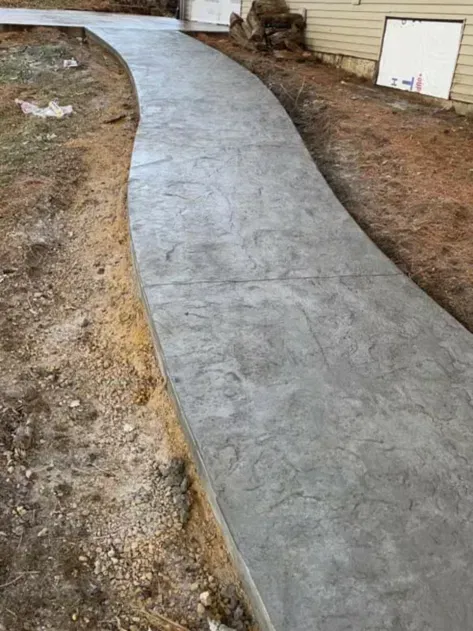 New concrete walkway curving beside a house in a dirt yard