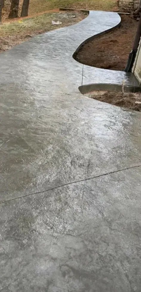 Curved concrete walkway in a wooded outdoor area after rain, with wet sheen and muddy edges