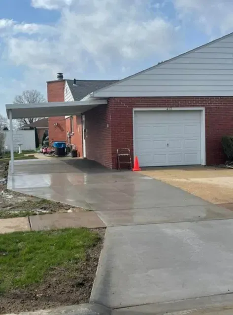Brick house with white garage door and wet concrete driveway under a cloudy sky.
