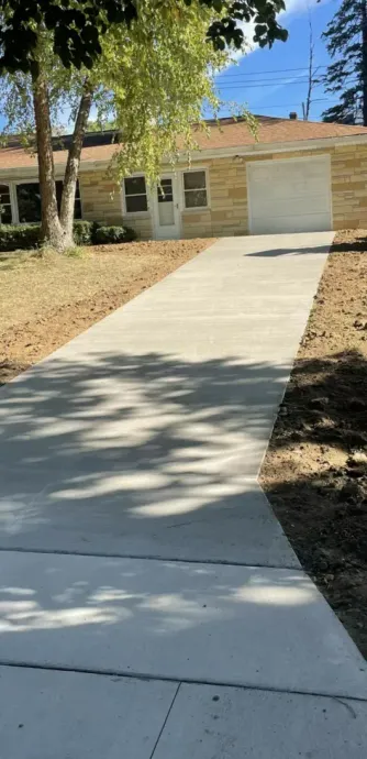 Concrete driveway leading to a single-story house with a garage and shaded front yard.
