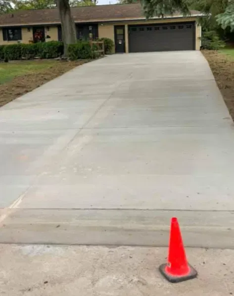 Concrete driveway leading to a garage, with a red traffic cone near the bottom right.