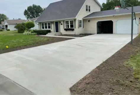 New concrete driveway beside a beige house with attached garage and lawn