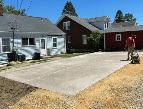 Fresh concrete driveway between two houses; worker with a power trowel smoothing the surface on the right