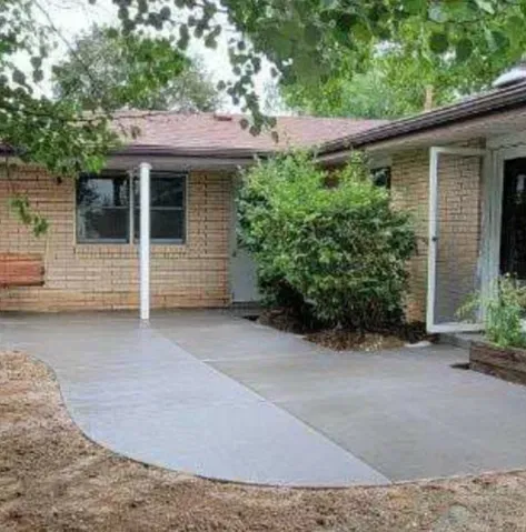 Front porch with a gray accessible ramp leading to a brick house entrance, bordered by shrubs and trees