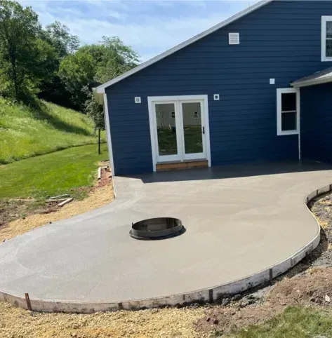 Curved concrete patio beside blue house with a round fire pit in the center