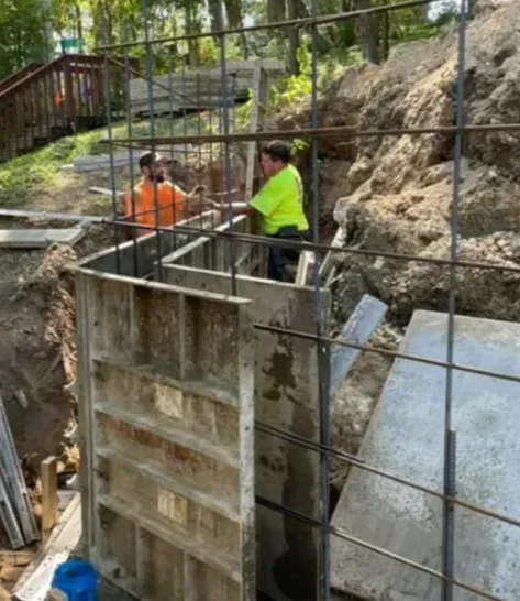 Workers in orange and neon shirts on a construction site beside a concrete wall and rocky slope